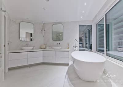 Wide shot of the bathroom with the tub, window views and french shutters