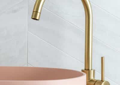 North beach coastal barn bathroom with brass tapware, pink concrete basins, v groove panelled cabinetry and onyx stone look tiles with a feature chevron pattern