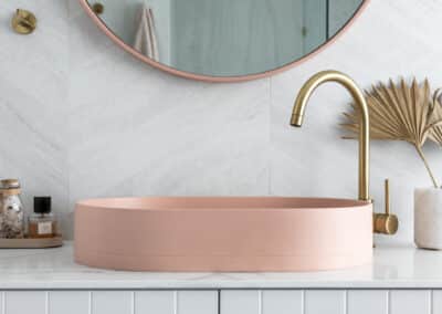 North beach coastal barn bathroom with brass tapware, pink concrete basins, v groove panelled cabinetry and onyx stone look tiles with a feature chevron pattern