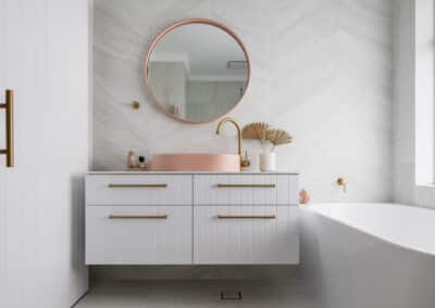 North Beach Coastal Barn Bathroom with brass tapware, pink concrete basins, V Groove panelled cabinetry and Onyx stone look tiles with a feature chevron pattern