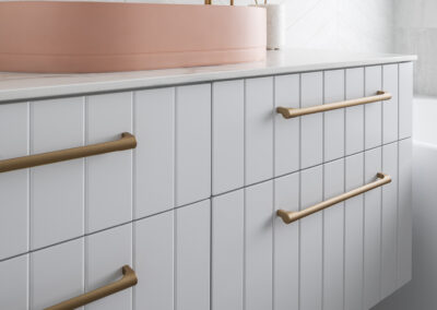 North Beach Coastal Barn Bathroom with brass tapware, pink concrete basins, V Groove panelled cabinetry and Onyx stone look tiles with a feature chevron pattern