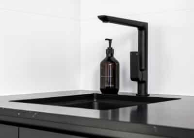 Monochrome laundry black tapware and black undermount sink on black engineered stone benchtop