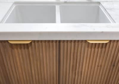 Porcelain sink with marble benchtop and scalloped timber cabinetry.