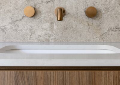 Close up of bronze tapware above the walnut vanity and organic white Caesarstone benchtop