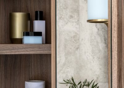 Close up of mirrored cabinetry open with products inside, in the reflection a Mona brass light