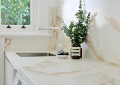 Contemporary warm marble look bookmatched benchtop and splashback and seamless light cabinetry for the new renovated laundry close up of sink and tapware