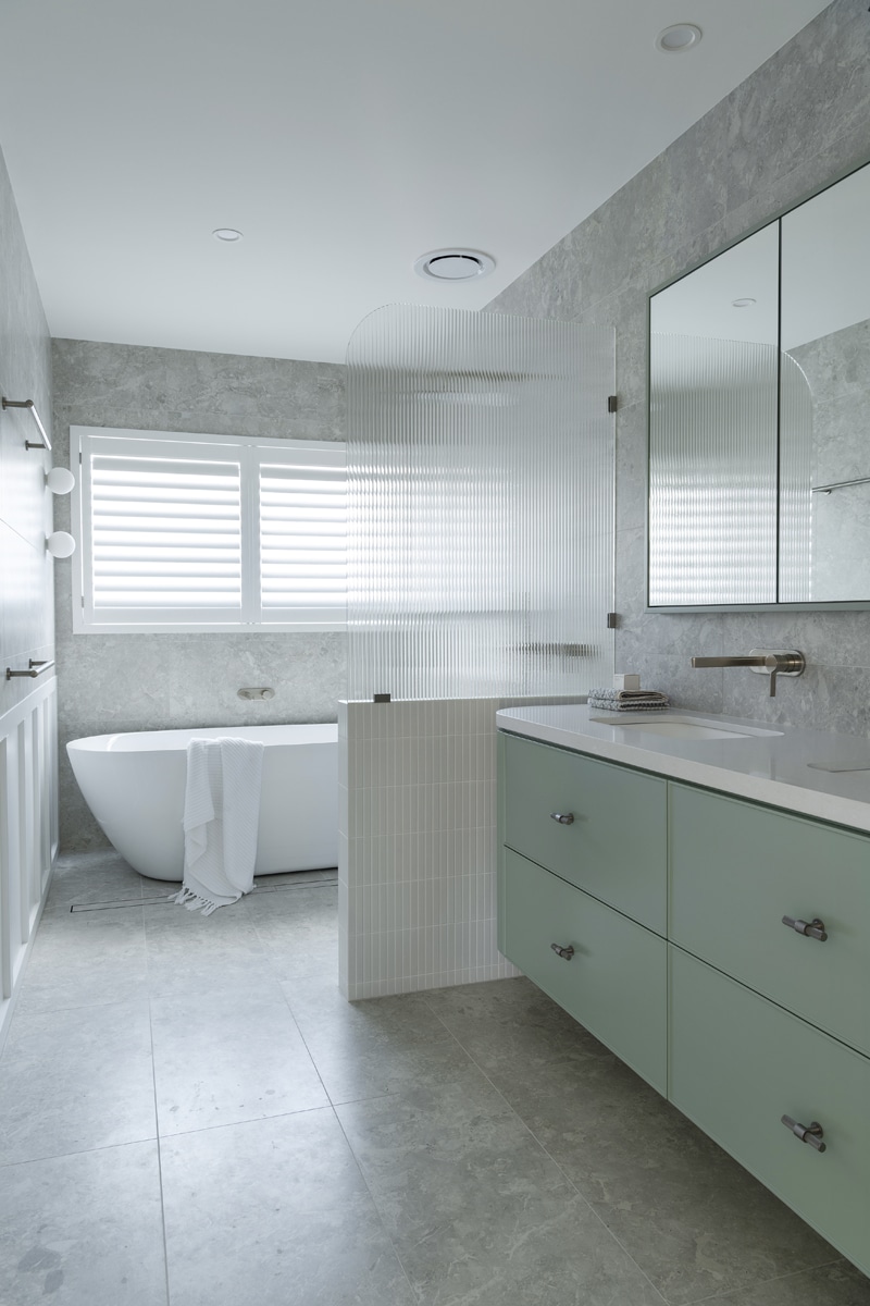 North beach coastal barn bathroom with brass tapware, pink concrete basins, v groove panelled cabinetry and onyx stone look tiles with a feature chevron pattern